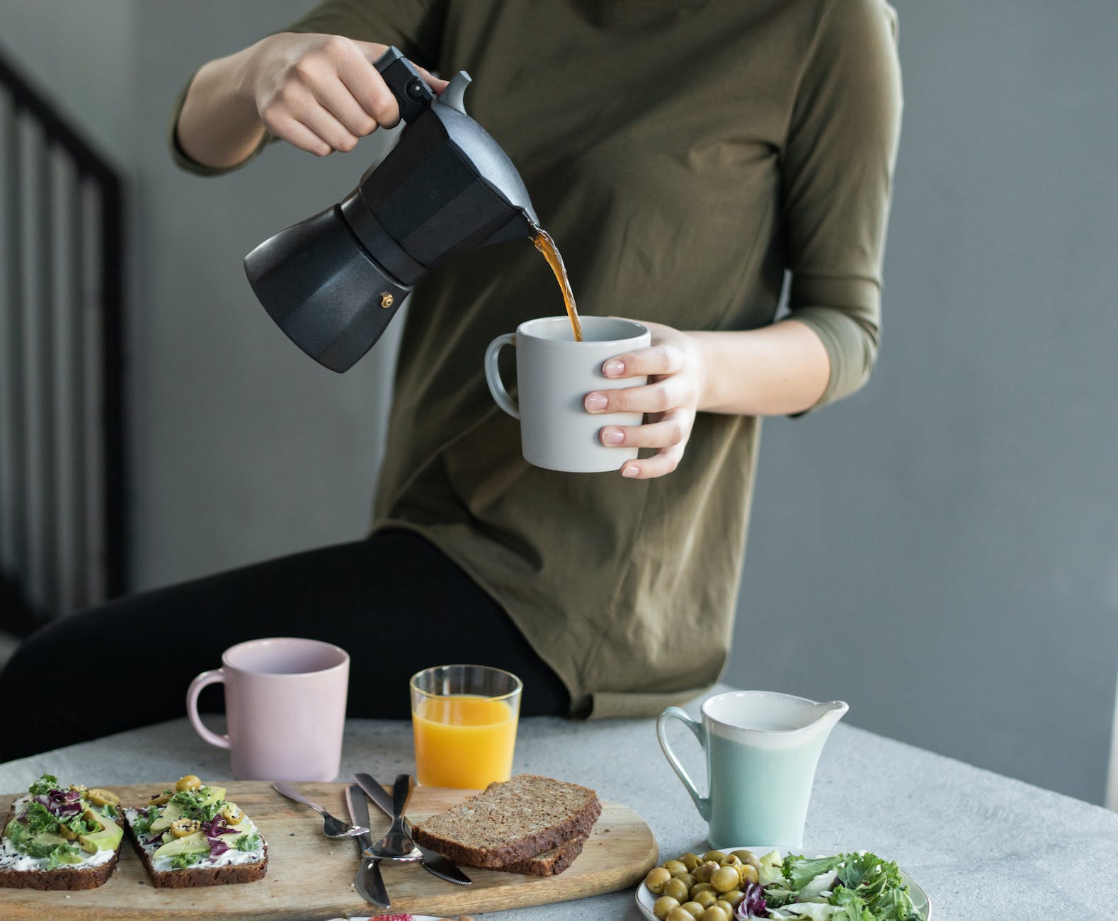 woman in green top pouring coffee in a white mug