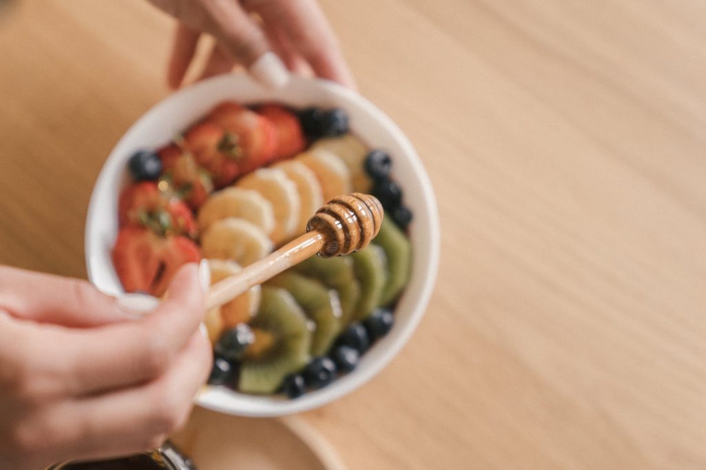 close up of woman pouring honey to fruits salad