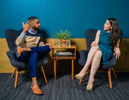 woman wearing teal dress sitting on chair talking to man