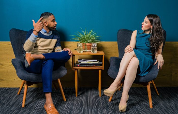 woman wearing teal dress sitting on chair talking to man