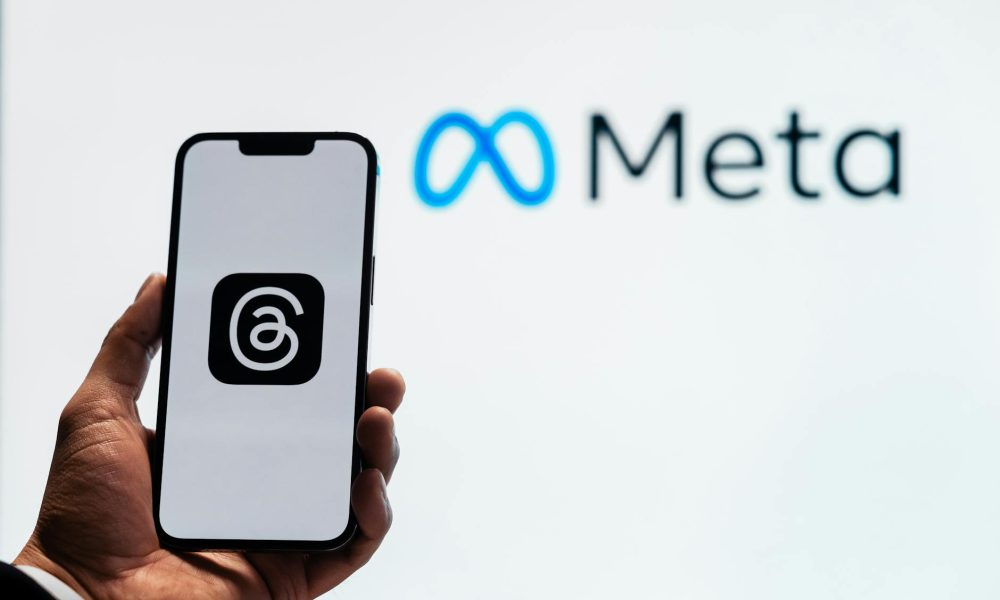 holding a smartphone with the threads app with the meta platforms logo in the background